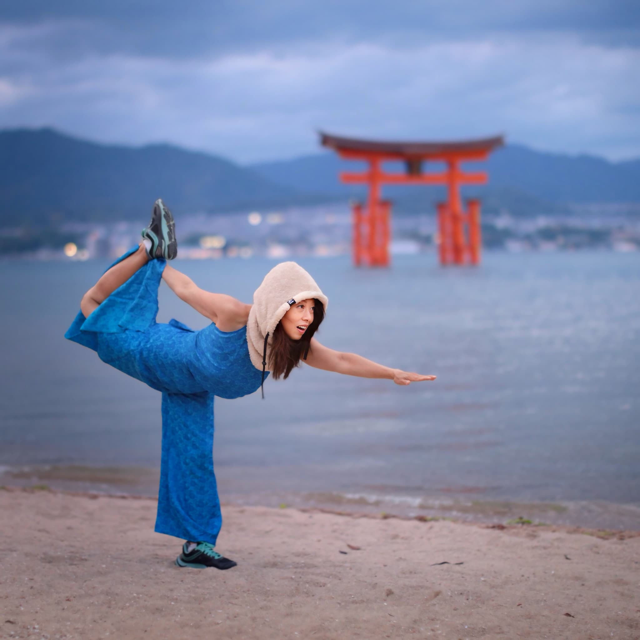 Nicole Pham balancing in dancer pose on a beach, the floating torii gate of Miyajima behind her